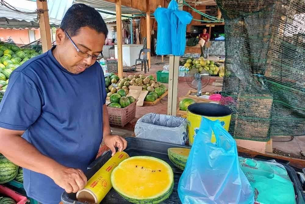 Salahuddin membungkus tembikai kuning dibeli pelanggan di gerai buahnya di Balok pada Selasa.