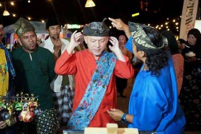 Razali (tengah) mencuba sarung alas kepala atau tanjak sempena Program 'Moreh Selepek Sahur' di Payang Walk di Kuala Terengganu.