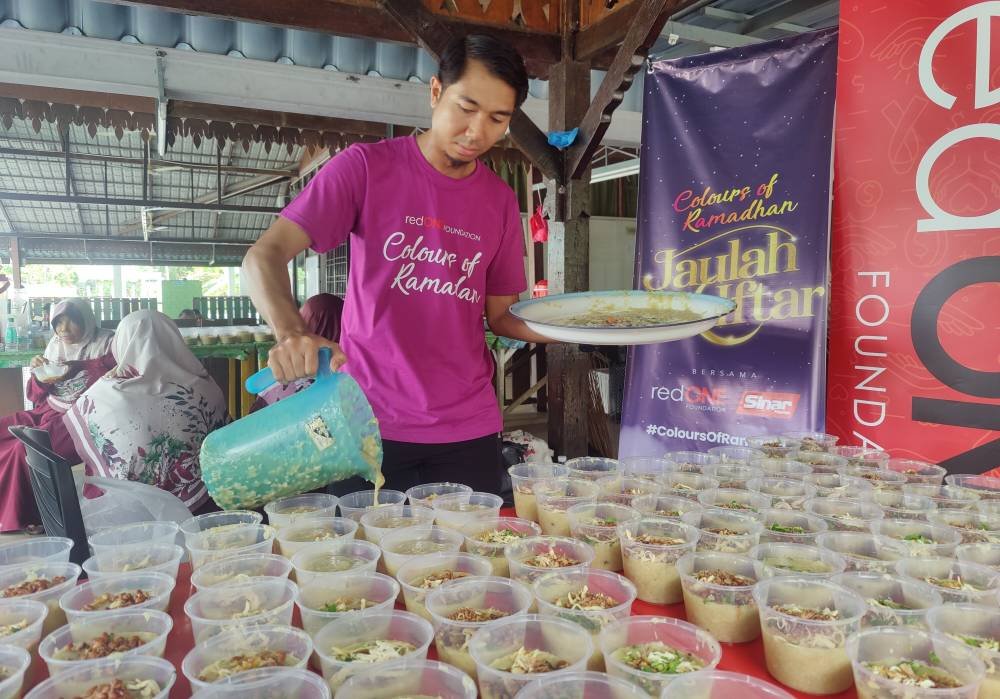 Seorang kakitangan redONE Mobile memasukkan bubur lambuk ke dalam bekas sebelum diedar kepada komuniti setempat.