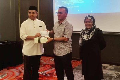 Mohamad Yusli (tengah) menyampaikan cenderahati kepada salah seorang penerima pada Program Nur Ramadan: Menyantuni Media dan Pendayung Santuari Kelip-Kelip Kampung Kuantan pada malam Khamis.