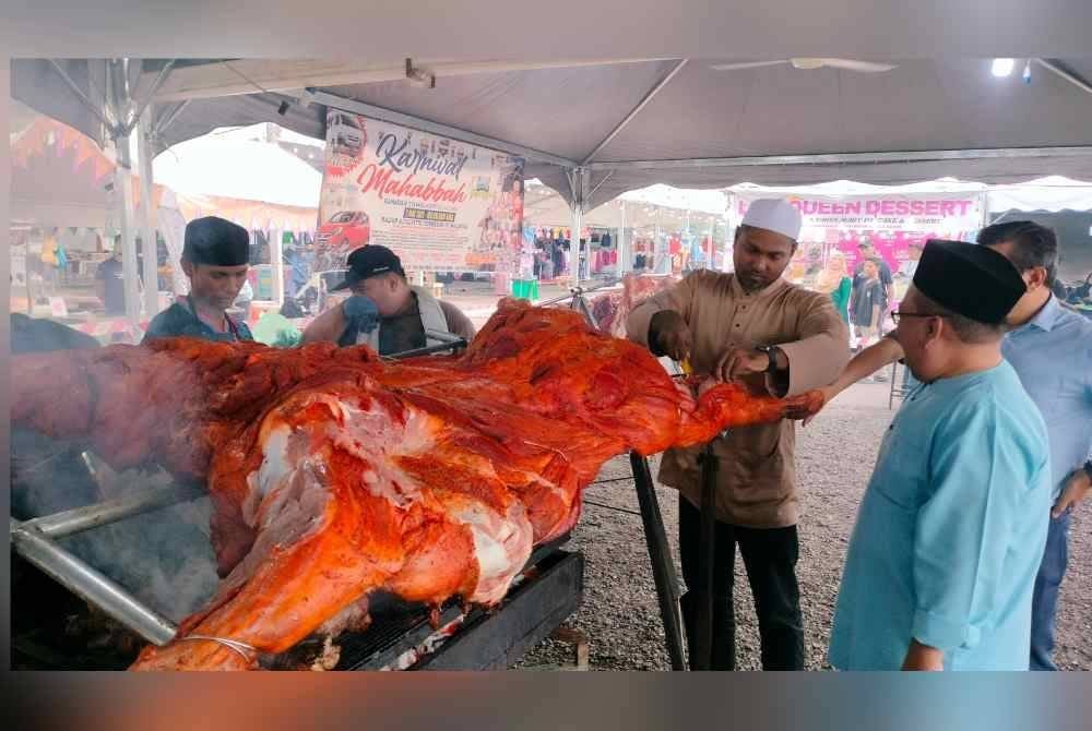 Zaini (kanan) melihat proses memasak lembu golek yang disediakan di Karnival Mahabbah,pada Jumaat.