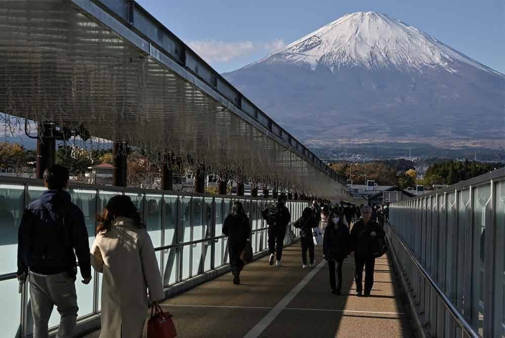 Orang ramai berjalan di atas jambatan yang menghubungkan kedai-kedai di sebuah pusat beli-belah outlet popular di bandar Gotemba, wilayah Shizuoka, dengan berlatar belakang Gunung Fuji. Foto AFP