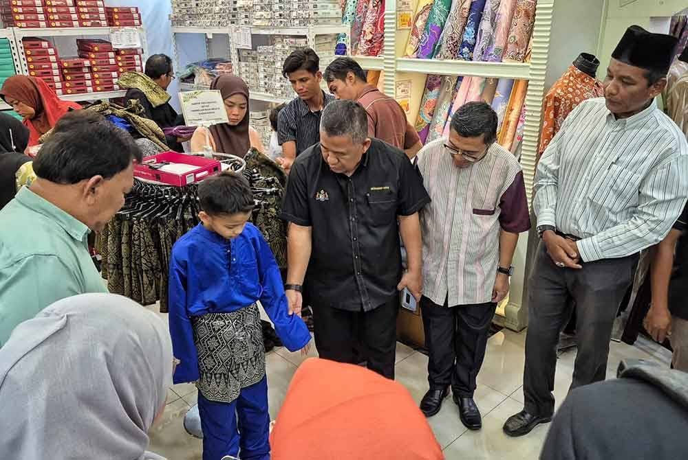 Mohamad Azmi (tengah) melihat seorang murid mengenakan baju raya pada program itu.