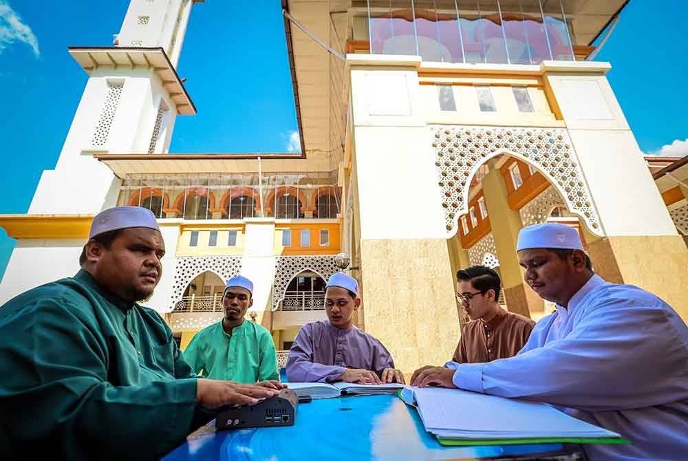 Ahmad Qusairi (kiri) bersama beberapa orang pelajar meluangkan masa mereka dengan membaca al-Quran Braille mashaf Malaysia sempena Nuzul Quran di pekarangan Masjid Darul Quran Jakim pada Selasa. Foto Bernama