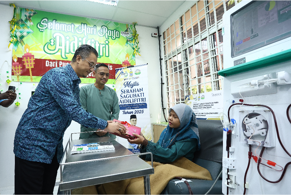 Mohamad (kiri) menyerahkan sumbangan duit raya kepada salah seorang pesakit buah pinggang di Pusat Hemodialisis Zakat Lebuh Buckingham pada Selasa.