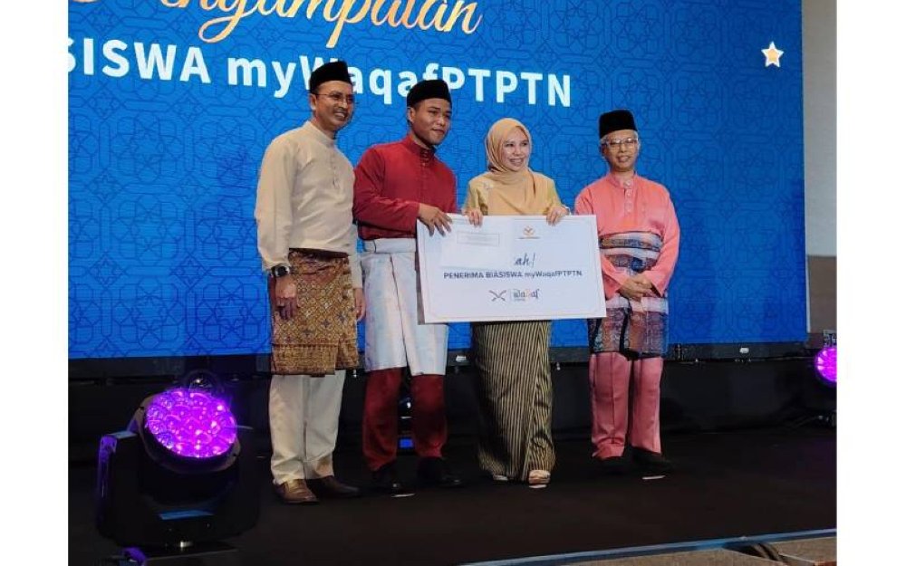 Norliza diiringi Ahmad Dasuki (kiri ) serta Dr Ridzwan (kanan) menyampaikan biasiswa myWaqafPTPTN kepada salah seorang penerima.
