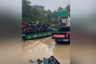 Treler membantu penunggang motorsikal yang terperangkap dalam banjir di bandaraya Johor Bahru.- Foto tular