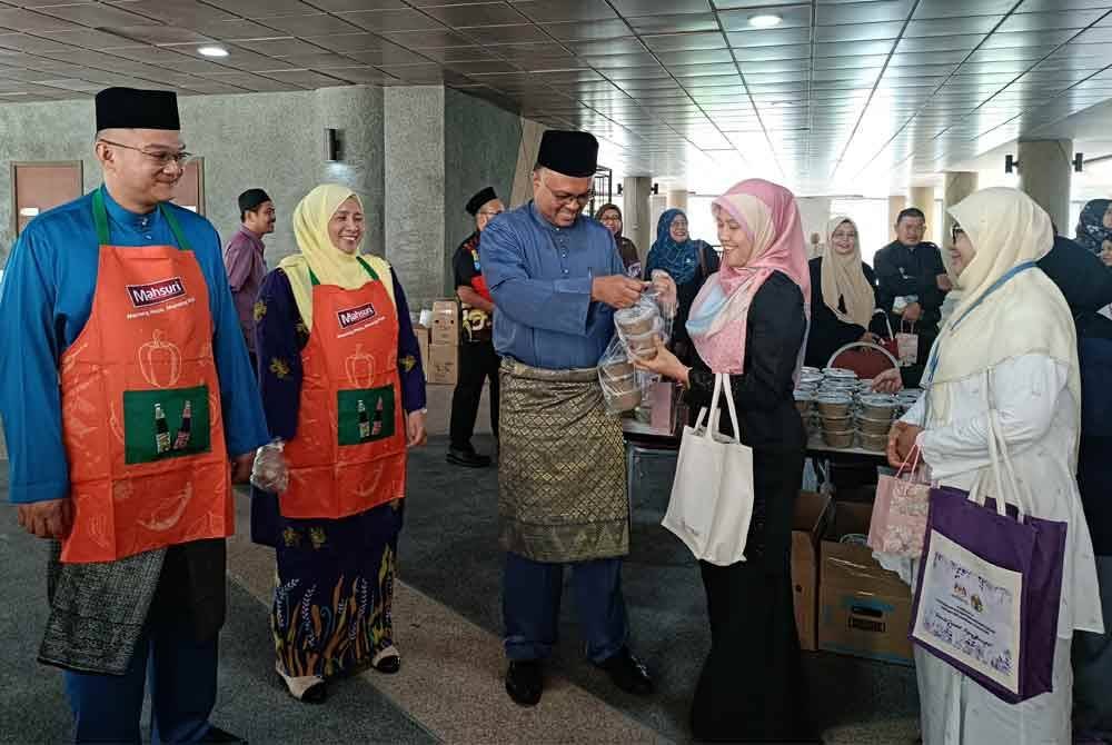 Isham (tengah) mengagihkan bubur lambuk kepada kakitangan KPKM di pekarangan Dewan Serbaguna Wisma Tani, KPKM pada Jumaat.