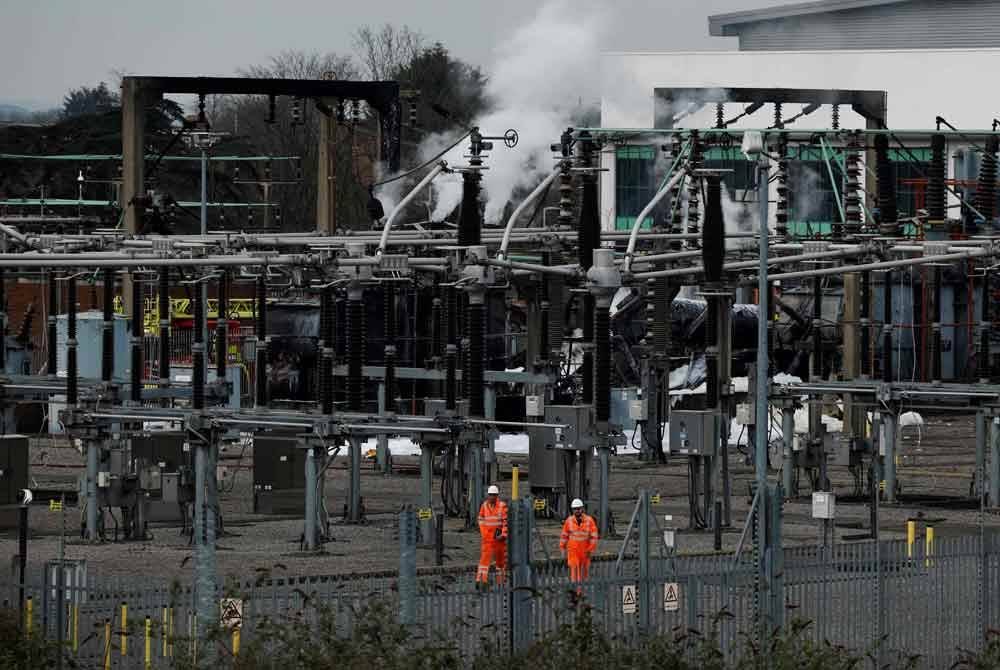 Beberapa kakitangan berjalan melewati stesen janakuasa yang masih berasap di Hayes, London barat, yang membekalkan tenaga ke Lapangan Terbang Heathrow, selepas kebakaran berlaku pada 21 Mac 2025. Foto AFP
