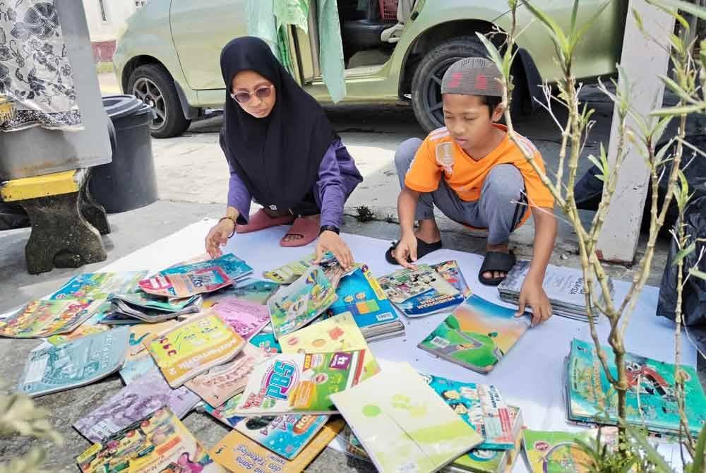 Besek Noor Ermita bersama anaknya memilih buku-buku yang masih elok dan tidak terjejas akibat rumah mereka dinaiki air baru-baru ini.