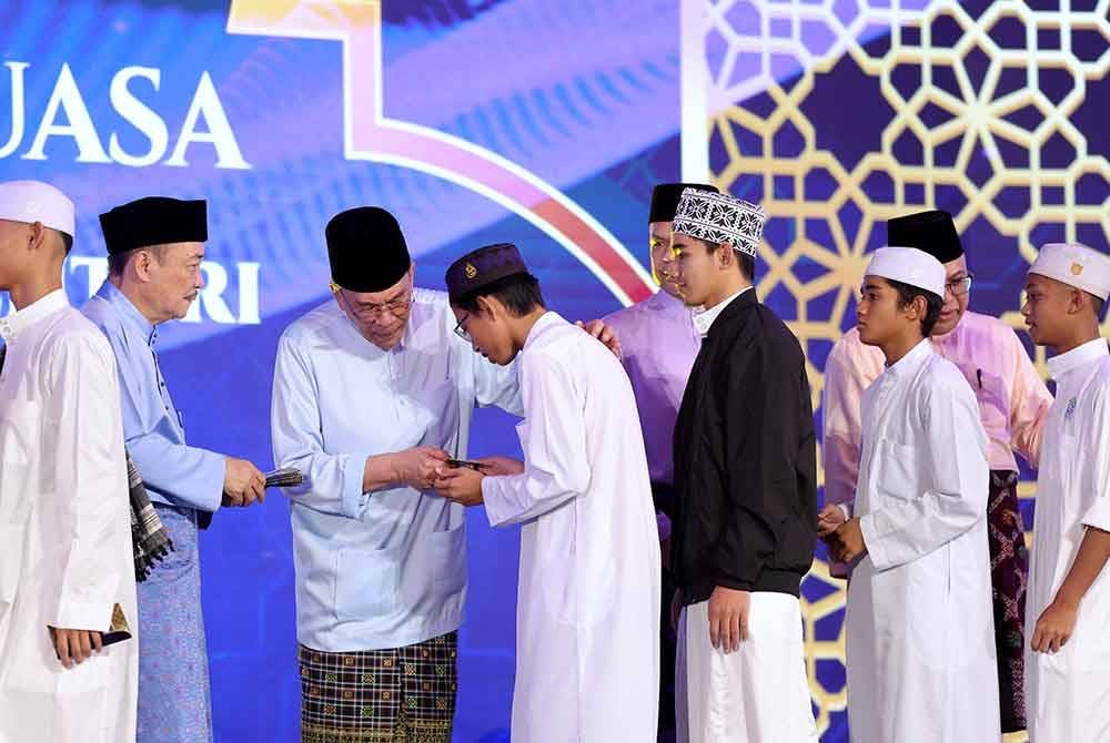 Anwa (tiga, kiri) diiringi Hajiji ketika menyampaikan sumbangan kepada para pelajar tahfiz pada Majlis Berbuka Puasa Madani Peringkat Negeri Sabah di Padang Tuaran pada Sabtu. Foto Bernama