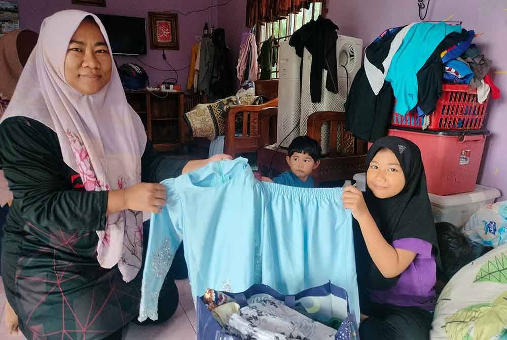 Nor Hamizah (kiri) menunjukkan bajur raya sempat diselamatkan ketika banjir pada Khamis.