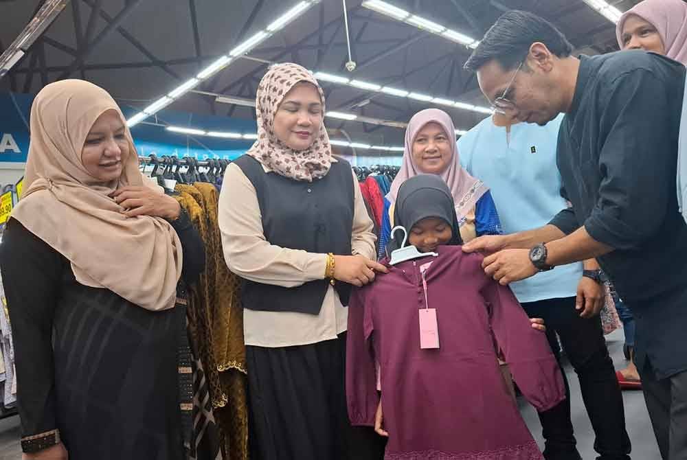 Mohd Azlan (kanan) membantu Nur Qasrina Qalesya Abdul Rahman,10, memilih pakaian baru sempena program Meriah Beraya Sejahtera Bersama 2025 di Pasar Raya Mydin, Pusat Transformasi Luar Bandar (RTC) Perak di Gopeng pada Ahad.