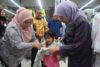 Nancy (kanan) memakaikan pakaian raya kepada salah seorang penerima sumbangan Program Sinar Syawal YKN 2025 di Kuching pada Ahad.