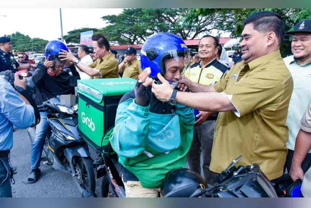 Shahelmey memakaikan helmet kepada penunggang motosikal sempena musim perayaan di Teluk Dumpil, Jalan Meruntum, Putatan.