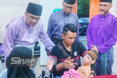 Amizar (kiri, berdiri) menyantuni pasangan suami isteri, Mohd Nor bersama isteri dan anaknya ketika Program Memacu Kehidupan: Hari Raya Aidilfitri oleh Yayasan Petronas di Dewan Semai Bakti Felda Kemasul pada Ahad.