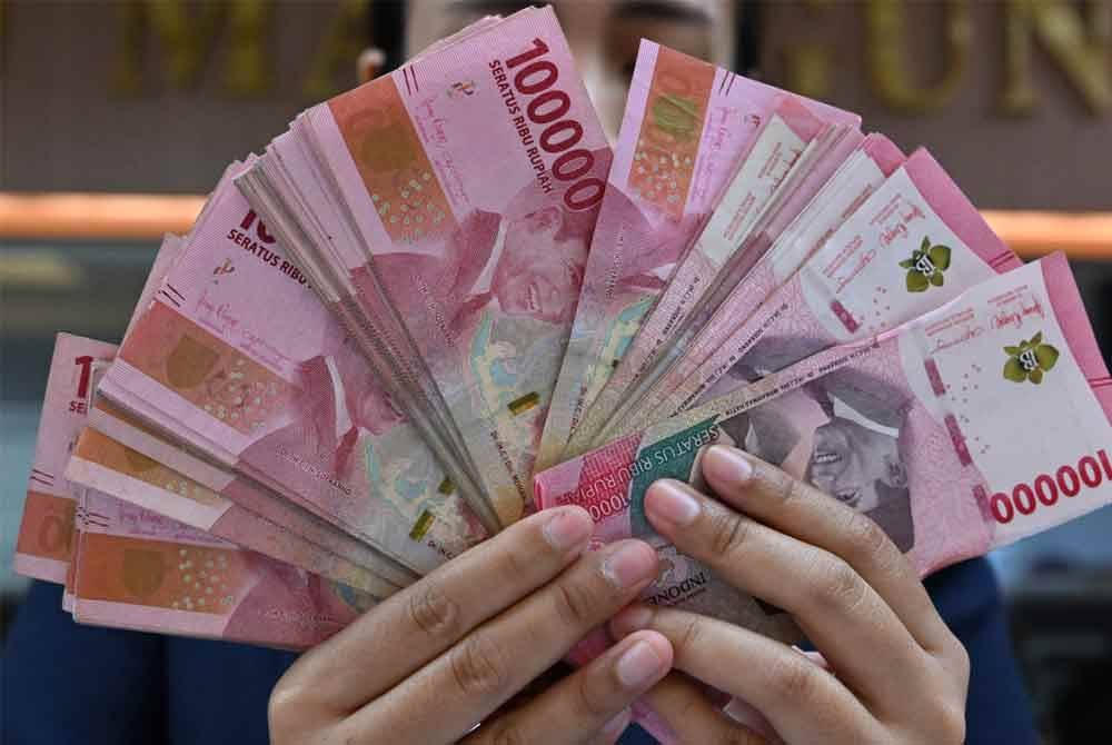 Seorang petugas di sebuah pusat pertukaran wang di Jakarta mempamerkan wang kertas rupiah Indonesia. - AFP