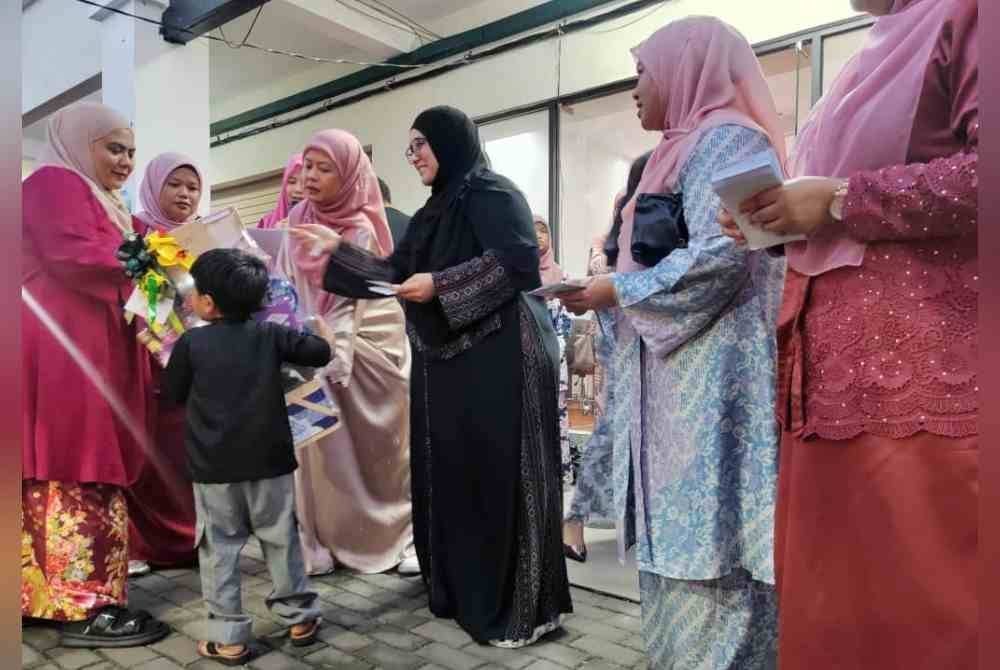 Mas Ermieyati (tiga dari kiri) dan Roseniza (dua dari kiri) menyampaikan sumbangan kepada salah seorang kanak-kanak yang diraikan pada Majlis Iftar Bersama Anak Yatim di Pusat Khidmat Srikandi Bersatu Melaka di Tambak Paya pada Jumaat.