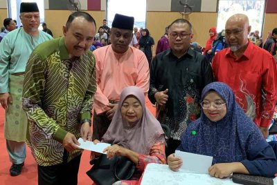 Mohd Jafni (kiri) menyampaikan sumbangan RM3,000 kepada ketua isi rumah yang terjejas banjir di Dewan Pejabat Daerah Kulai pada Khamis.