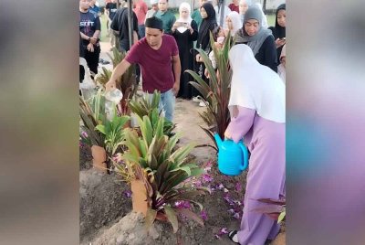 Ahli keluarga menyiram air di pusara tiga beranak yang dikebumikan dalam satu liang lahad di Tanah Perkuburan Islam Makam Dagang, Kampung Makam pada Jumaat.