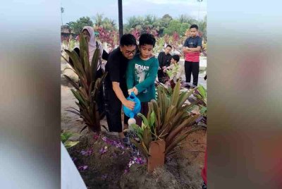 Salah seorang anak pasangan berkenaan, menyiram air di pusara ibu bapanya yang dikebumikan dalam satu liang lahad di Tanah Perkuburan Islam Kampung Makam.