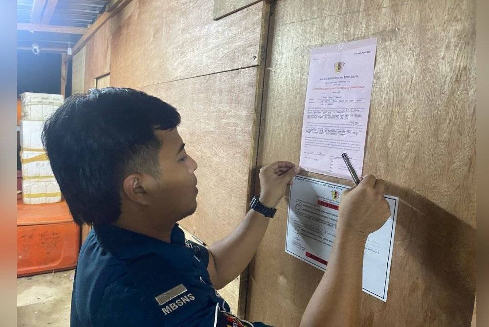 Penguat kuasa MBS menampal notis tutup premis di rumah kongsi yang dijadikan kedai runcit. Foto Veerapan