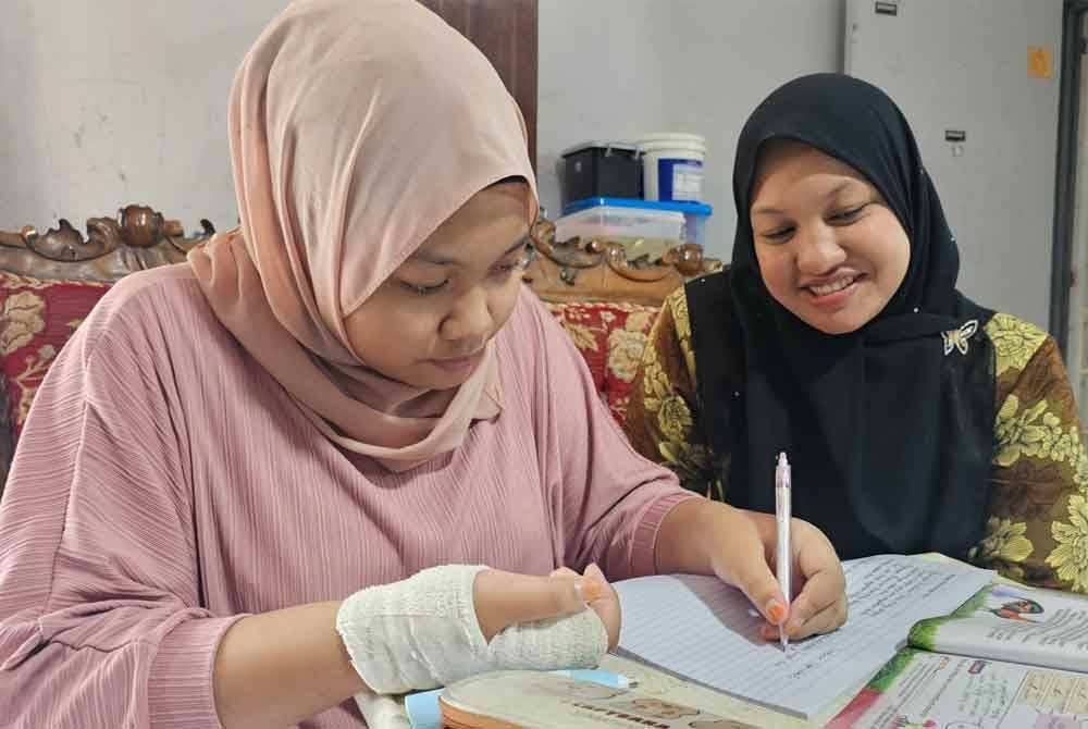 Nasuha Batrisyia yang mengalami kecederaan di tapak tangan kini berlatih menulis menggunakan tangan kiri sambil diperhatikan oleh ibunya, Nor Azira.