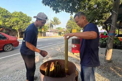 Jeffrey (kanan) menyediakan perkakasan untuk membakar lemang di dalam tong drum.