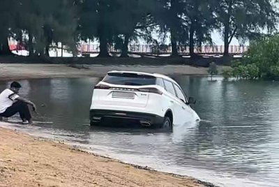 Gambar tular seorang lelaki dilihat duduk di atas batu disamping Proton X70 yang terbenam di dalam air laut