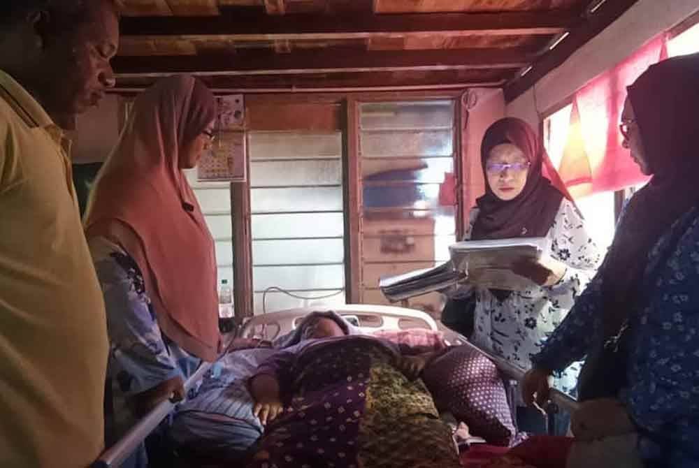Zuraini (dua dari kanan) melihat rekod rawatan ketika menziarahi Afifah di Kampung Pulai Cengai, Gurun.