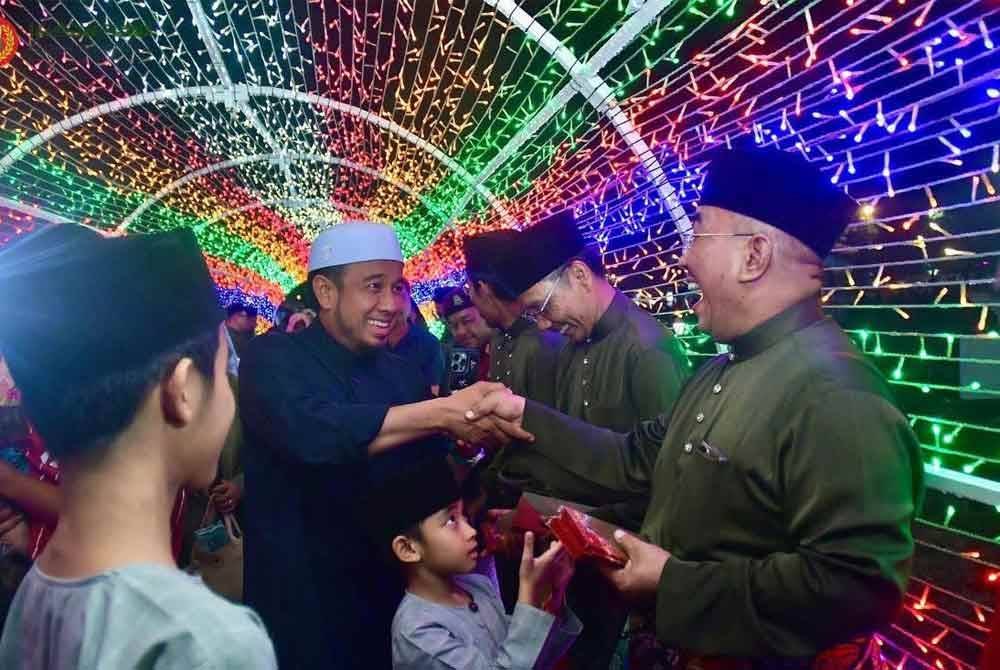 Muhammad Sanusi (kanan) memberikan duit raya kepada kanak- kanak yang menghadiri Majlis Rumah Terbuka Aidilfitri di Seri Mentaloon pada Ahad. - Foto UPDA