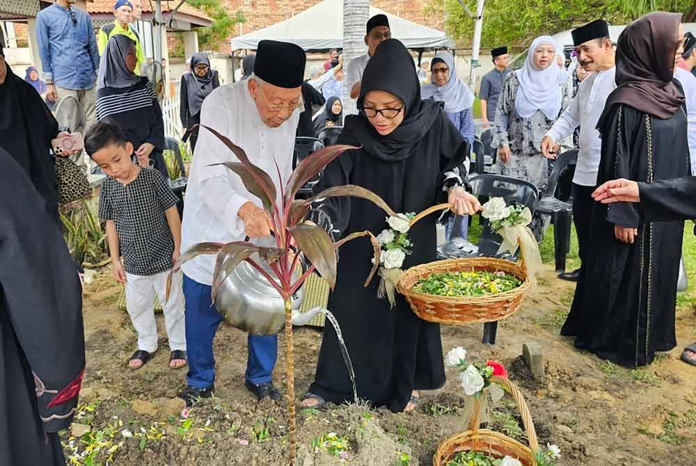 Nik Hussain (kiri) yang dibantu menantunya, Nur Zulaikha Azman, 35, menyiram pusara Noor Azizah selepas selesai pengebumian di Tanah Perkuburan Islam Masjid Paloh, Ipoh pada Isnin.