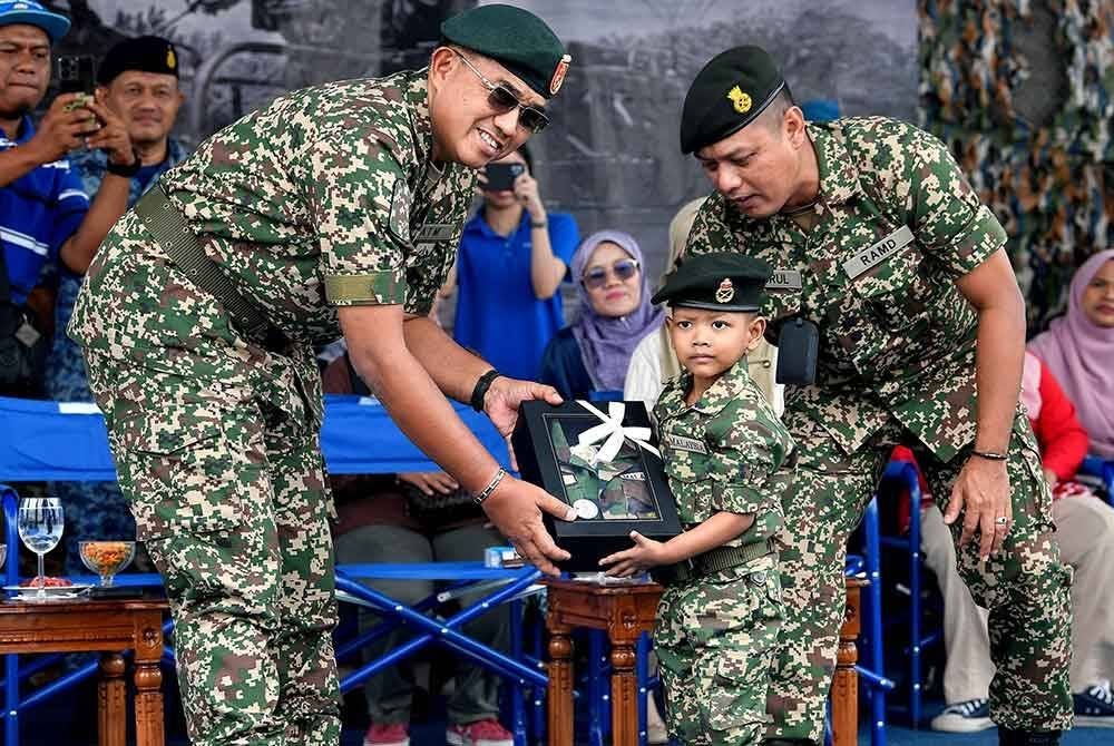 Panglima Angkatan Tentera Jeneral Datuk Mohd Nizam Jaffar (kiri) menyampaikan cenderahati kepada adik Akif Ziyan Azhar, 5, yang memakai uniform penuh anggota tentera ketika Program "Make A Wish" Kanak-Kanak Menghidapi Leukemia Bersama Angkatan Tentera di Padang Kawad Pangkalan Udara Jugra, Banting, pada Isnin. Foto Bernama