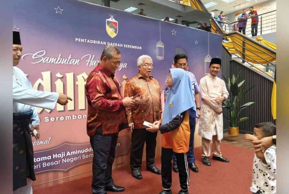 Aminuddin (kiri) menyampaikan sumbangan duit raya pada Sambutan Hari Raya Aidilfitri peringkat Pentadbiran daerah Seremban di Kompleks Pentadbiran Daerah Seremban 2 pada Selasa.