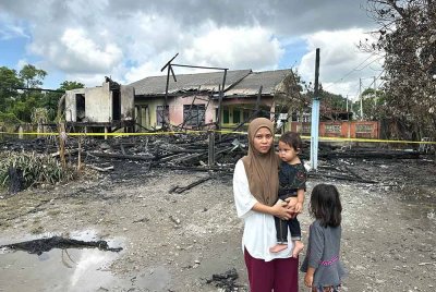 Nurul Waddah bersama dua anaknya melihat keadaan rumah yang terbakar dalam kejadian di Kampung Gelong Gajah, di Kuala Terengganu pada malam Selasa.