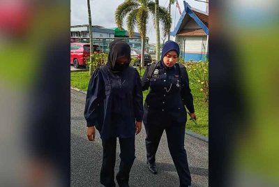 Tertuduh (kiri) diiringi polis tiba di Mahkamah Majistret Sungai Besar pada Khamis.