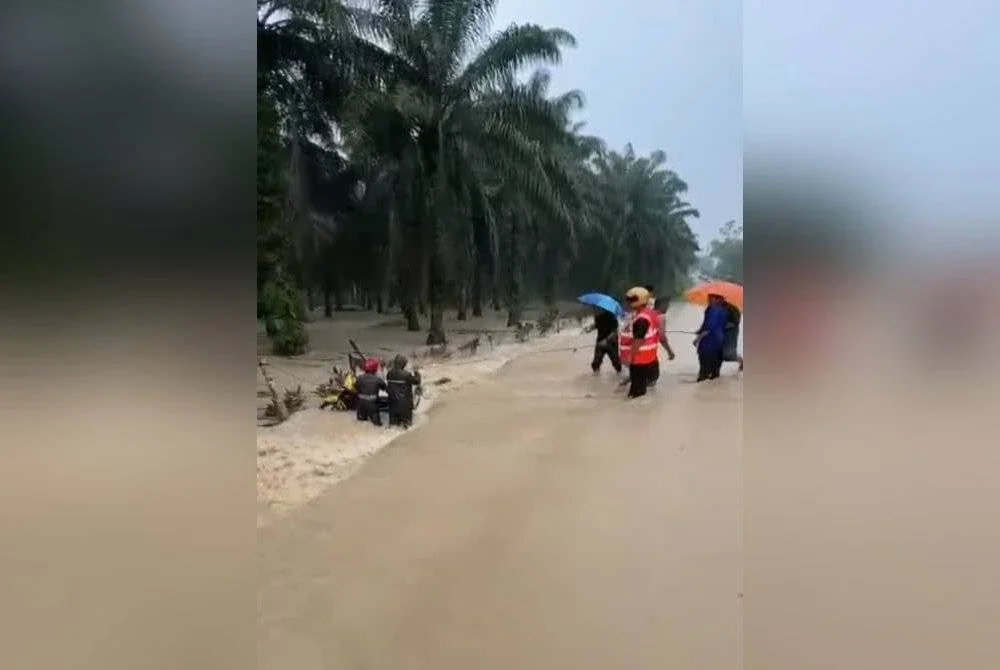 Orang ramai membantu menarik motosikal yang hanyut dibawa arus deras di jalan masuk Felda Air Tawar 3, pada petang Ahad. Foto tular