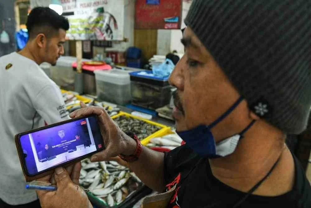 Peniaga ikan, Mohd Rozi Yahaya, 54, menyaksikan lintas langsung perjalanan terakhir Tun Abdullah. Foto Bernama