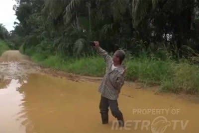 Penduduk berswafoto di jalan Desa Bukit Baling, Kecamatan Sekernan, Muaro Jambi yang berlubang dan digenangi air. - Agensi