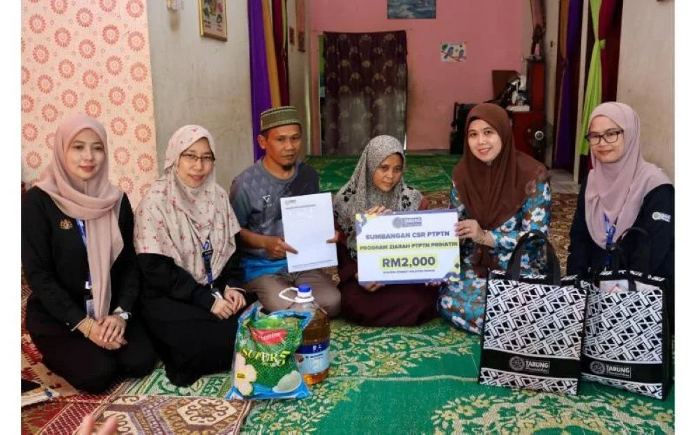 Wan Zawiah (dua dari kanan) menyerahkan replika kad sumbangan CSR PTPTN kepada ibu Allahyarham Manarina (tiga dari kanan) semasa Program Ziarah PTPTN Prihatin di Felda Chemplak, Labis.
