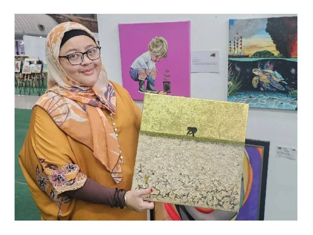 Rita memegang lukisan bertajuk When The Lands Stop Giving karya Salma Malihah.