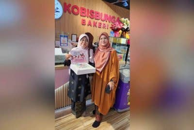 Pengasas Kobis Bunga Bakery, Norul Syafinas Abu Bakar (kanan) menyerahkan kek kepada wakil salah sebuah sekolah yang menerima kek berkenaan sempena sambutan Hari Guru.
