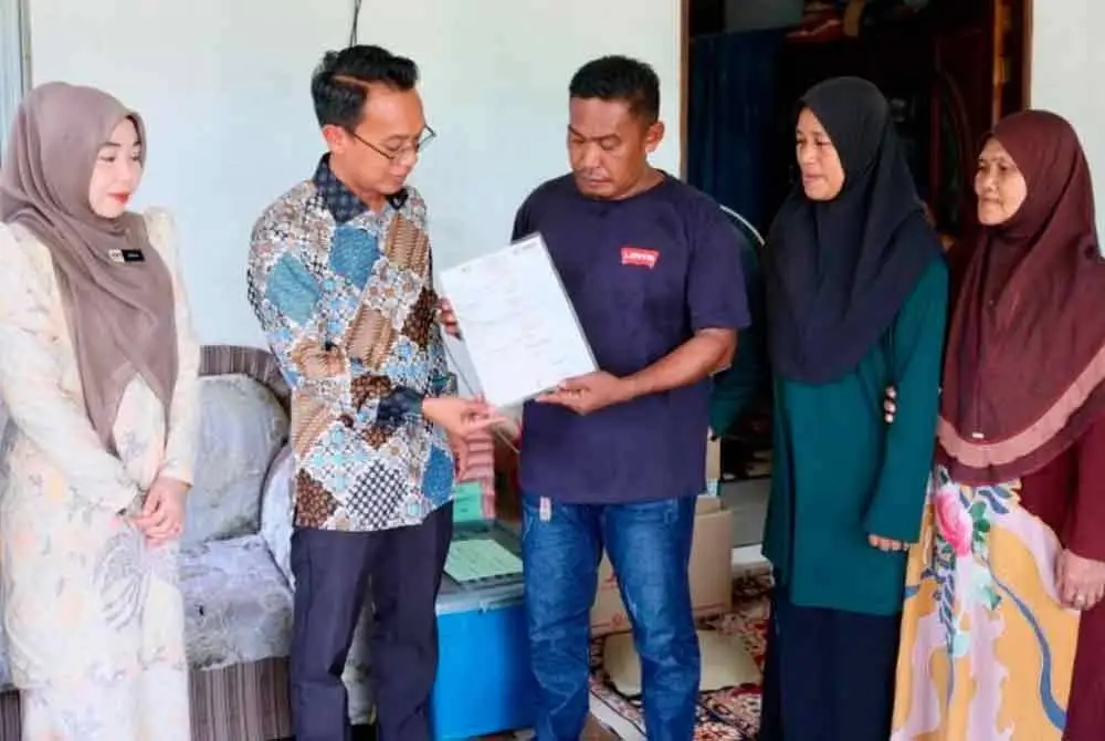 Mohamad Nasir (dua,kiri) menyerahkan sijil kematian kepada waris pelajar UPSI di Kampung Bharu Tok Dor, Besut pada Khamis.