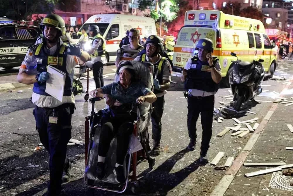 Seorang wanita yang cedera dibawa keluar dengan kerusi roda di Ramat Gan, Tel Aviv, selepas serangan peluru berpandu Iran. - AFP