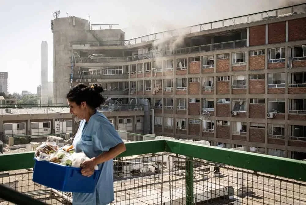 Seorang jururawat membawa bekalan perubatan melepasi bangunan yang terbakar di Hospital Soroka selepas serangan peluru berpandu Iran di Beersheba. - AFP