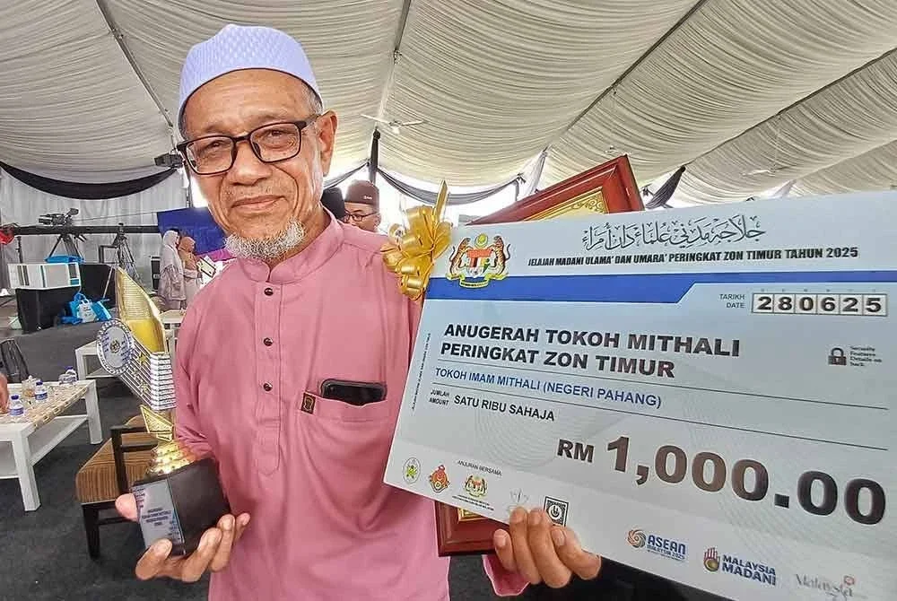 Mat Saman menunjukkan trofi dan replika cek yang diperolehnya selepas terpilih menerima Anugerah Tokoh Imam Mithali Program Jelajah Madani Ulama dan Umara Zon Timur bersempena Karnival Al-Falah Madani Indera Mahkota Pahang di Masjid Beserah di Kuantan pada Sabtu. Foto Sinar Harian.