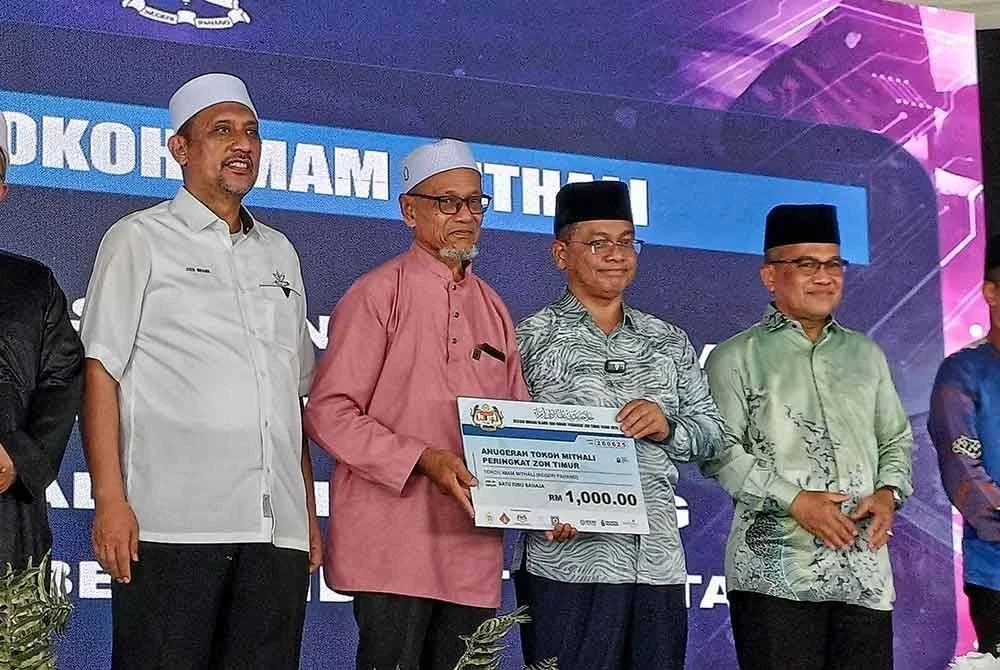 Mohd Naim menyerahkan replika cek kemenangan kepada Mat Saman selepas dipilih sebagai penerima Anugerah Tokoh Imam Mithali Program Jelajah Madani Ulama dan Umara (JMUU) Zon Timur bersempena Karnival Al-Falah Madani Indera Mahkota Pahang di Masjid Beserah di Kuantan pada Sabtu. Foto Sinar Harian.