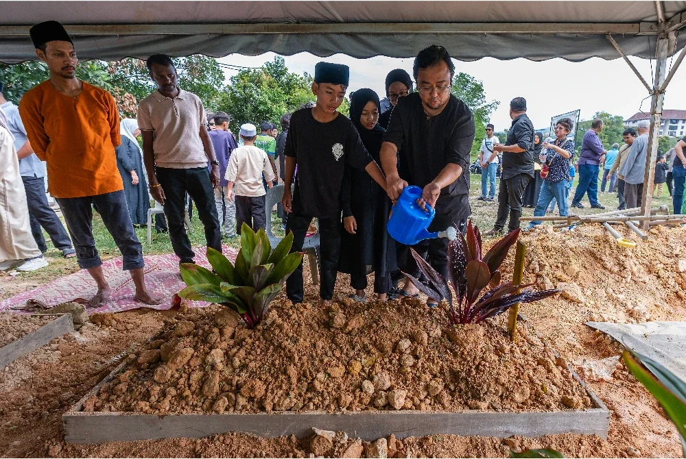 Ahli keluarga menyiram air pada pusara Muhammad Khairy Nunis selepas selamat dikebumikan di Tanah Perkuburan Islam Taman Sri Sinar Segambut pada Ahad. Foto Bernama