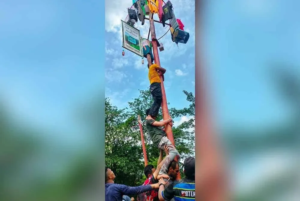 Peserta berusaha memanjat batang pinang licin yang menawarkan pelbagai hadiah menarik.