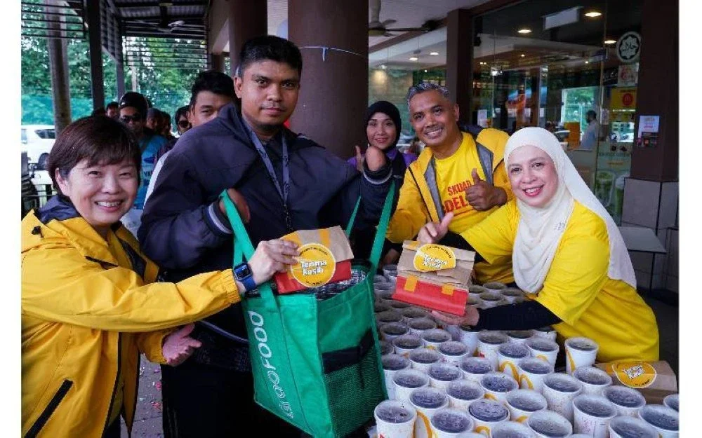 Melati (kanan) menyerahkan set hidangan percuma kepada penghantar makanan sempena kempen #MekdiBelanjaRider di McDonald’s Bandar Sri Damansara pada Selasa.